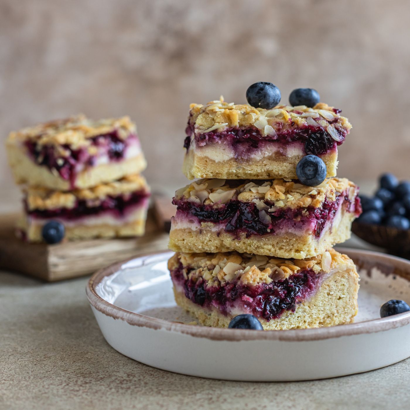 Crumble-cheesecake-bars-with-blueberry-filling-and-fresh-blueberries,-concrete-background.-Bar-slices-with-cheesecake,-blueberry-and-streusel.-1336151149_2125x1416 square.jpeg