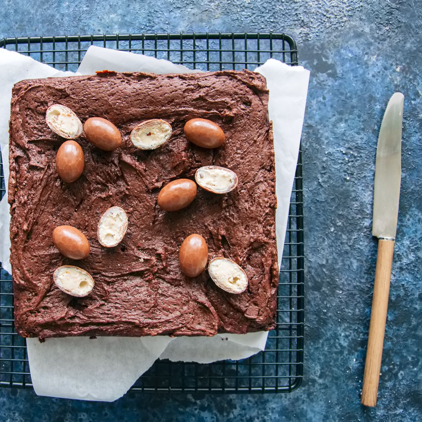 Dark-chocolate-brownie-squares-on-a-wire-rack-decorated-with-creamy-chocolate-eggs.-Blue-stone-background.-949443858_4288x2848 square.jpeg