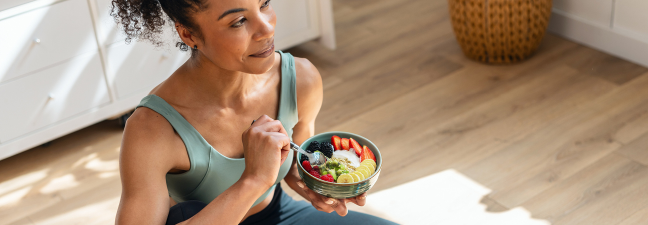 Athletic woman eating a healthy fruit bowl while sitting on floor in the kitchen at home Athletic woman eating a healthy fruit bowl while sitting on floor in the kitchen at home